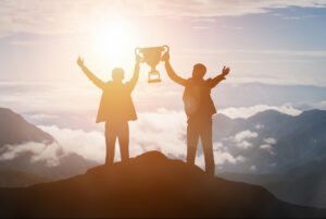 zwei Menschen mit Pokal auf der Spitze eines Berges